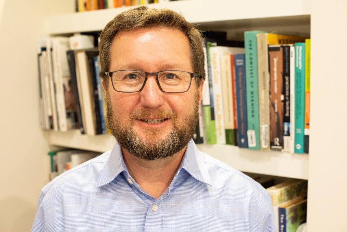 Dr Richard Duggins smiling in front of a bookshelf